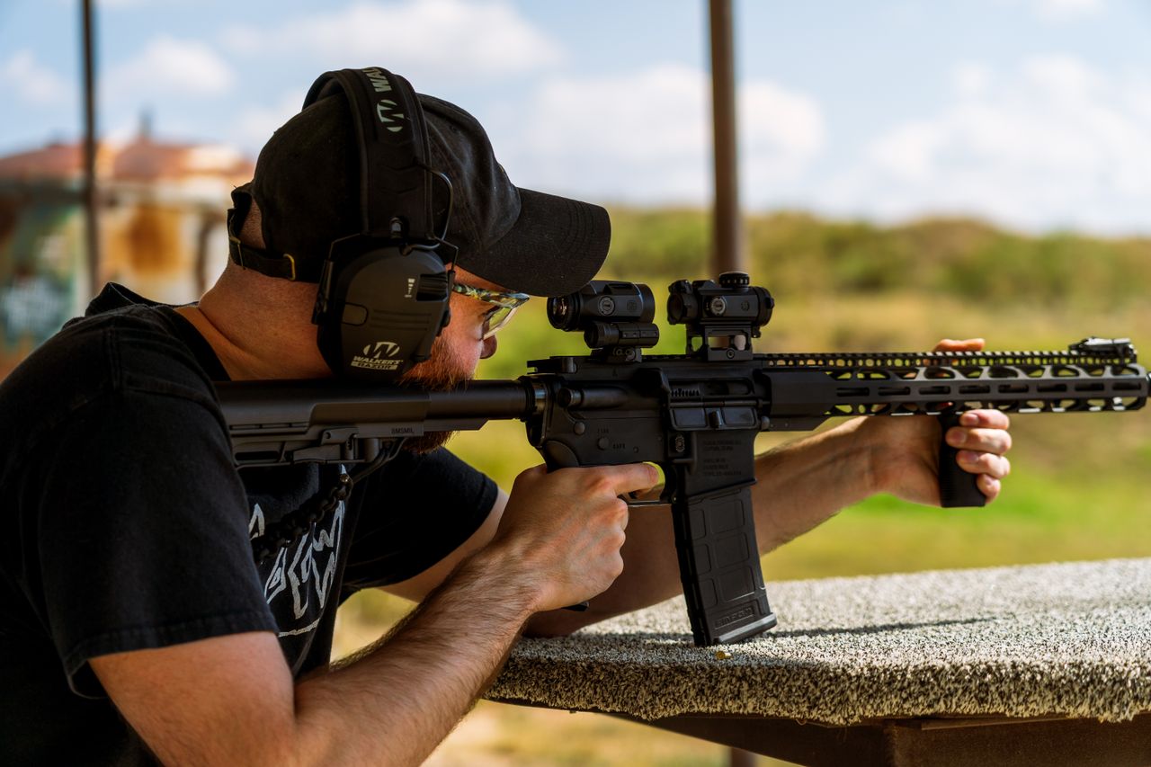 Mastering the First Impression: Your intriguing post title goes here Adult male aiming with a rifle at an outdoor shooting range. Daytime setting with clear skies.